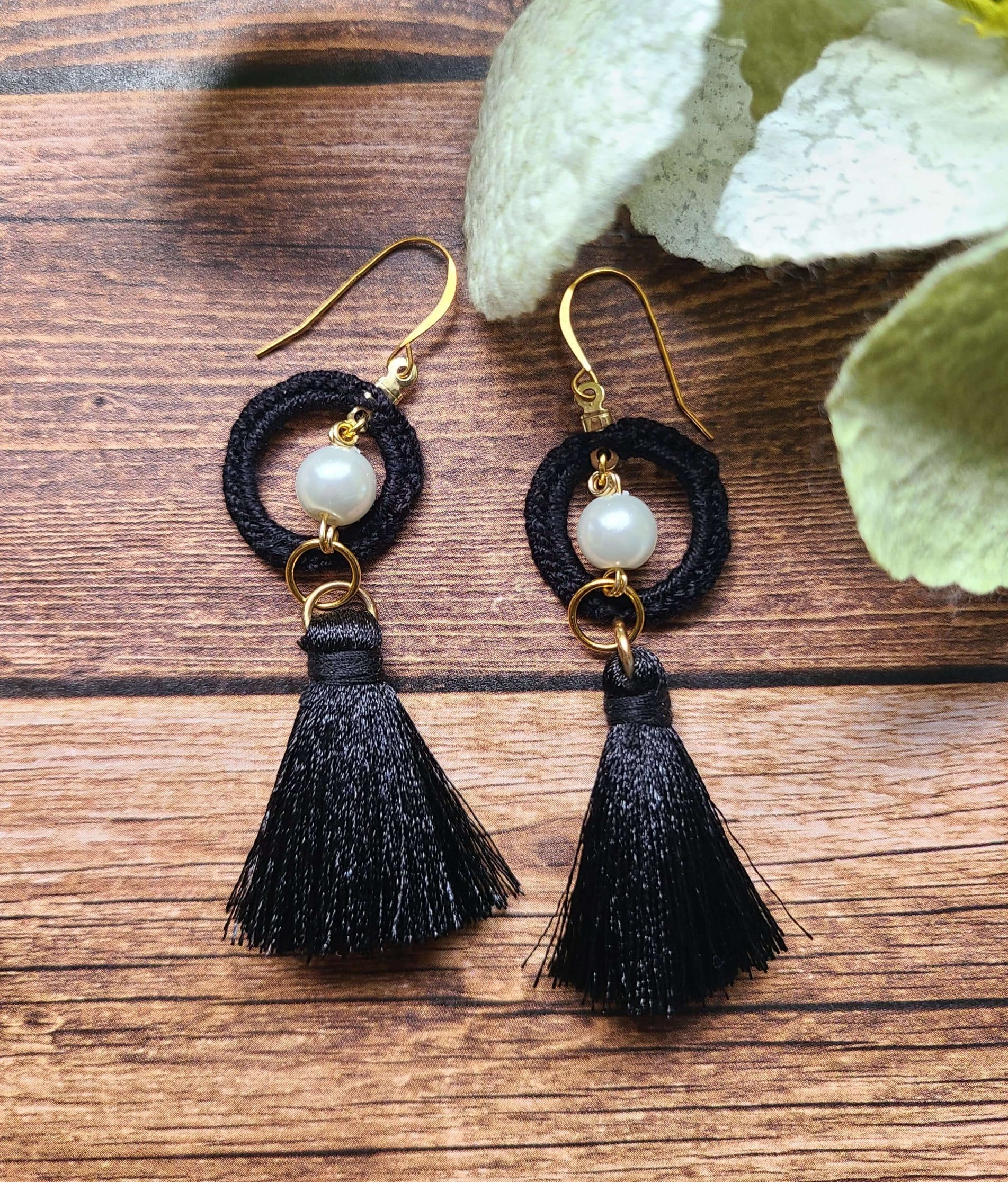 Black tassel pearl earrings on a wooden background.