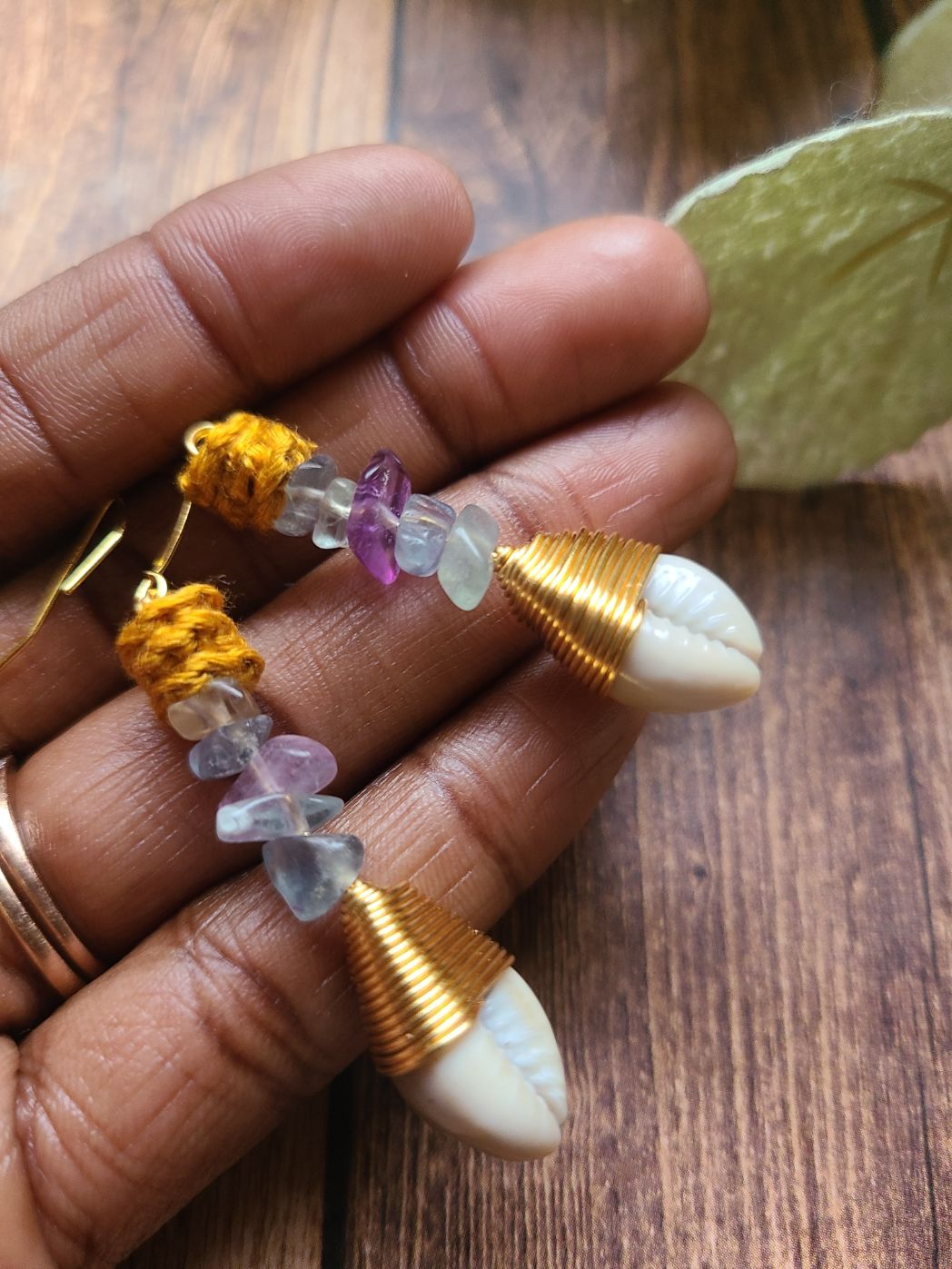 Holding a pair of fluorite dangle earrings with gold wire wrapped cowrie shells.