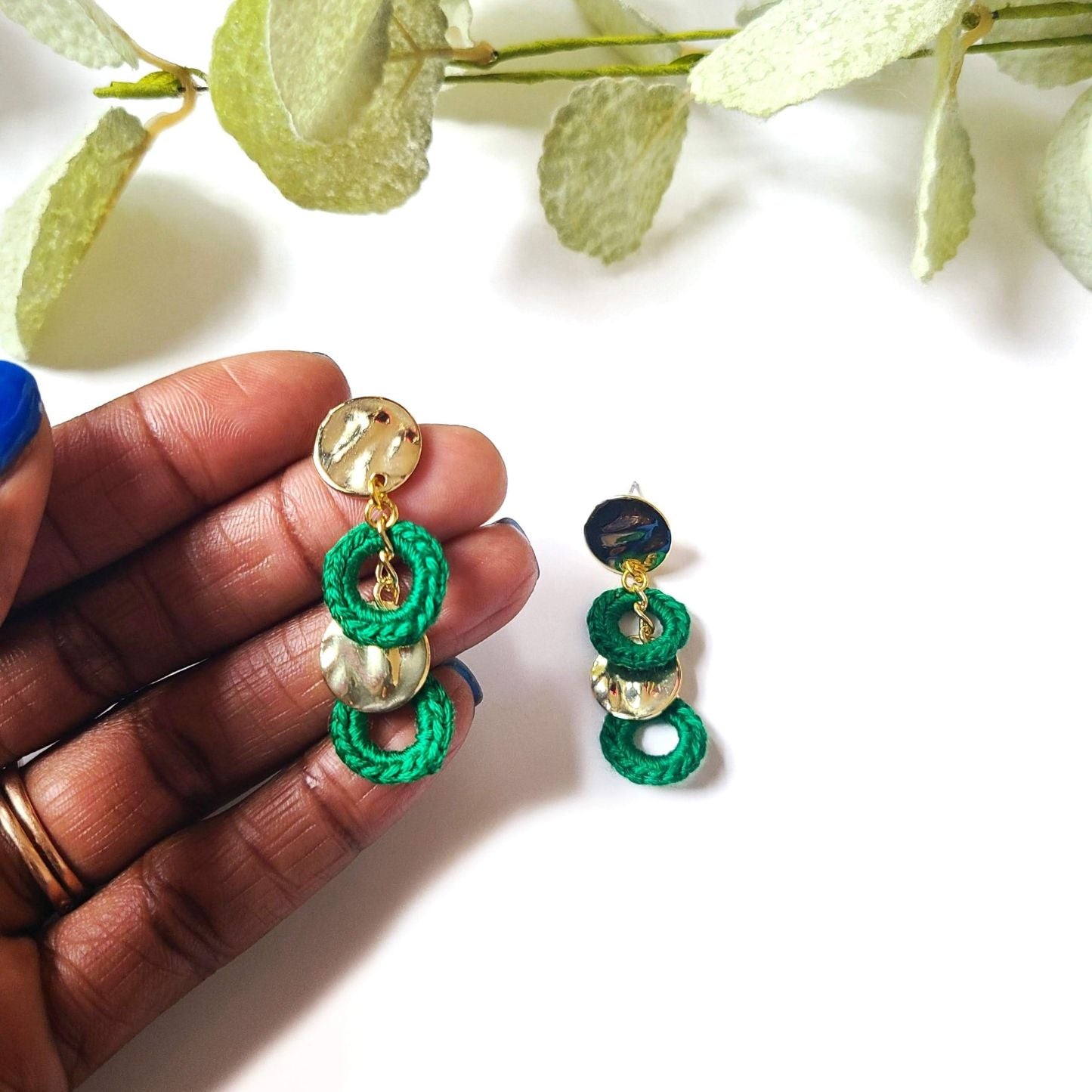 A model holding a pair of gold and green circle earrings.