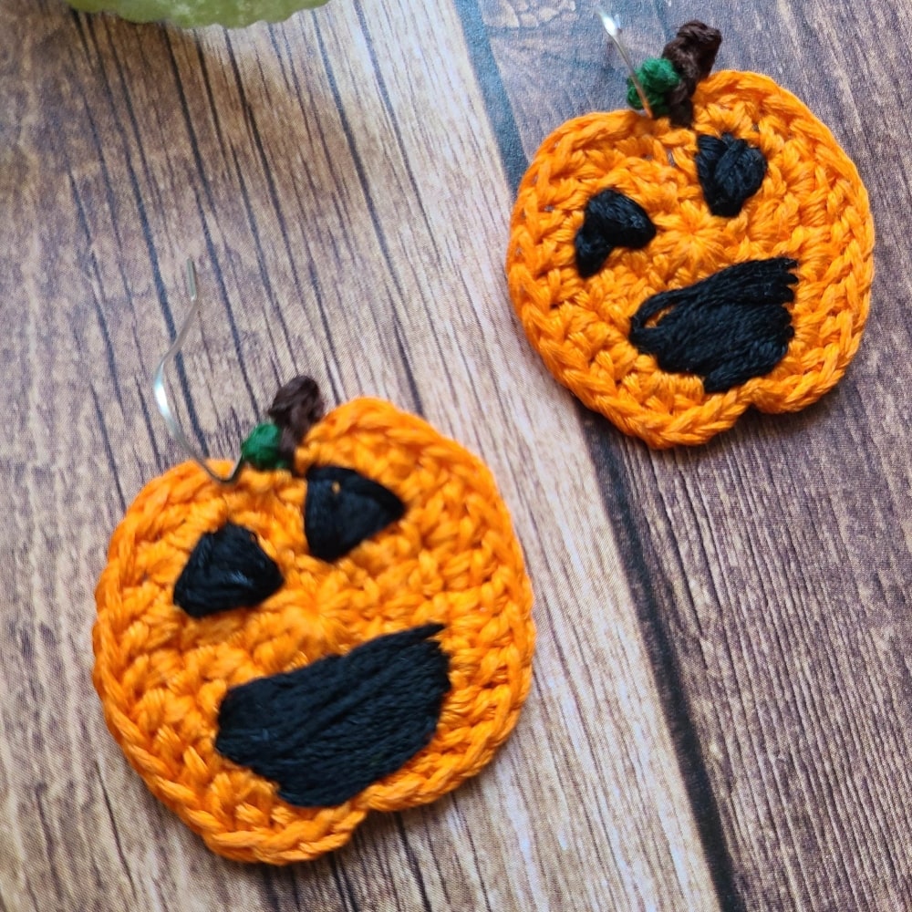 Pumpkin earrings that are Halloween dangle earrings on a wood background.