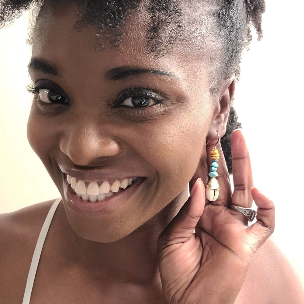 Model wearing Wagnerite Turquoise earrings that dangle with a cowrie shell